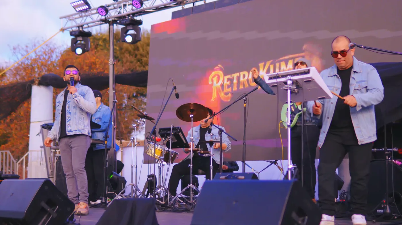 La banda completa tocando en un escenario al aire libre